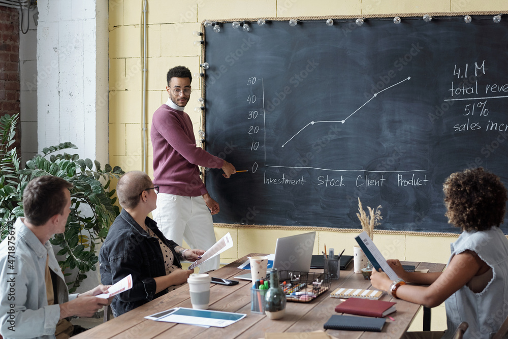 Aufkleber Young confident coach pointing at blackboard with graph drawn with chalk while presenting it to colleagues at seminar