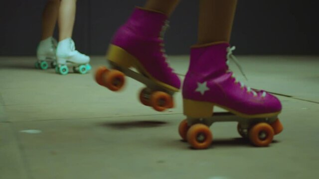 Female legs in roller blades, skating fast at the roller park on floor . Close-up legs of young women is professionally skating . Different kind of and colorful vintage roller blades . Slow Motion