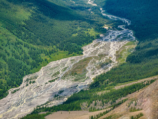 Glaciers melt, water flows into the valley. Picturesque highland green landscape with wide mountain river in valley. Awesome alpine view to motley mountain valley. Aerial view.