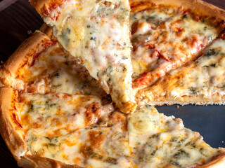 Close-up of a ready-made Italian pizza with four cheeses on a brown wooden background. A traditional dish of Italian cuisine. Home cooking. Take one of the slices. Selective focus