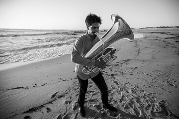 Man musician plays the tuba near the ocean. Black and white photo.