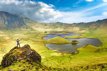 The landscape of Corvo Island in the Azores with man on rock peak with open arms. Concept of freedom and travel adventure.