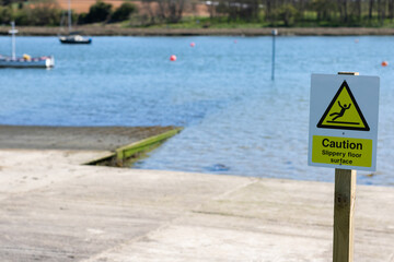 Warning sign for Slippery floor surface on a jetty by a river. The white & yellow sign also has clear picture symbol of man slip and fall on the top.
