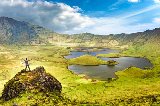 The landscape of Corvo Island in the Azores with man on rock peak with open arms. Concept of freedom and travel adventure.