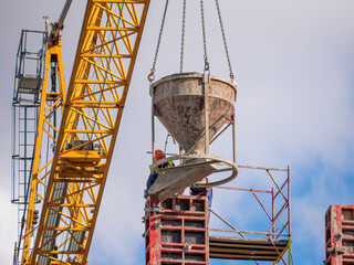 Builders pour concrete from the tank into the steel formwork. Monolithic construction of buildings. The crane holds the concrete container