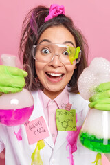 Vertical shot of positive Asian woman looks with glad surprised expression holds two glass beakers...