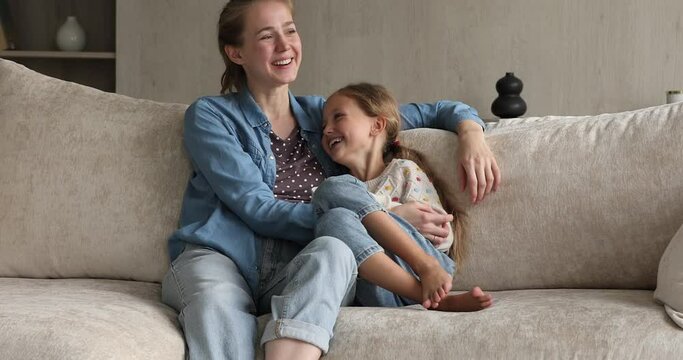 True love and devotion. Loving family of two foster mother and preteen adopted daughter cuddle on sofa at living room. Caring elder sister spend time with younger one talk feel emotional bonding laugh