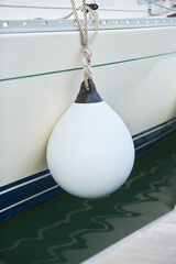 White fenders suspended between a boat and dockside for protection. Maritime fenders