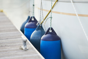 White fenders suspended between a boat and dockside for protection. Maritime fenders - obrazy, fototapety, plakaty