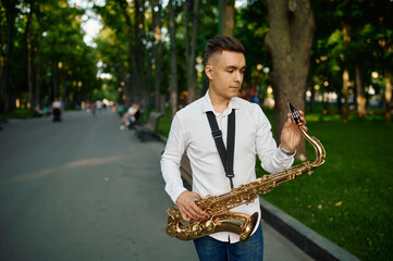 Young saxophonist with saxophone on alley in park