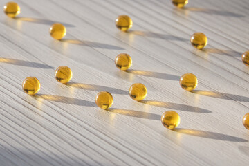 Gold pills. Close up photo of the scattering of amber-coloured fish oil tablets on the light surface. Therapeutic effect, pharmaceutics concept. Drugstore Theme. Copy space