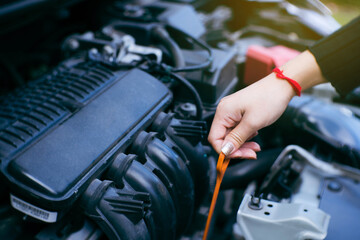 Close up of unrecognizable young woman's hand check oil level of car engine. Young Asian woman hand lowering dipstick measuring oil level of car engine before travel.