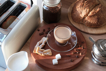 Top view of the still-life in the kitchen during breakfast with the jar of coffee, beans, cream pot, toaster, sugar bowl, sugar cubes, fresh homemade cakes, bread and cup of latte.