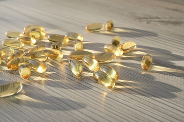 Gold pills. Close up photo of the scattering of amber-coloured oblong fish oil tablets on the light...
