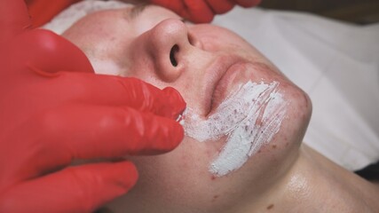 Application of a cream mask on the face of a girl with problem skin in the salon.