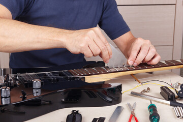 Guitar repairer checks leveling of frets on neck of modern guitar.