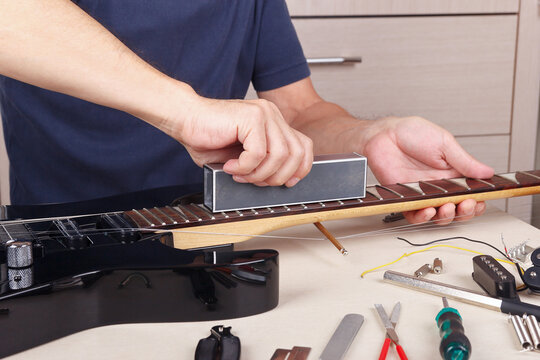 Guitar master aligns frets on guitar neck with leveling bar.