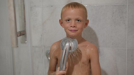 Portrait of a little emotional boy in the shower, water is pouring on him and he is smiling.