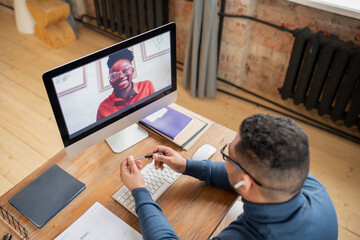 Happy young African female looking at her teacher from computer screen during discussion of subject of online lesson