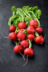 Red radish bunch with green leaves, on black stone background