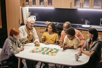 Large happy multiracial family of three generations playing board game while sitting by table in the kitchen - Powered by Adobe