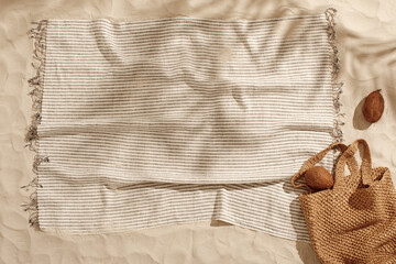 Striped linen beach towel with fringes, woven bag and two coconuts on sandy beach with shadows from...