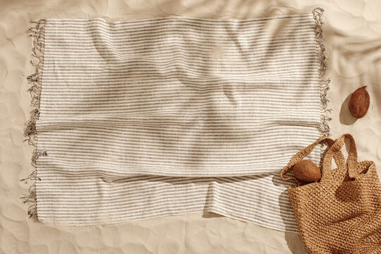 Striped linen beach towel with fringes, woven bag and two coconuts on sandy beach with shadows from palm tree. Relaxation and tropical summer holidays concept