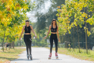 Obraz premium Full body portrait of happy sportswomen rollerskating in the park on a sunny day