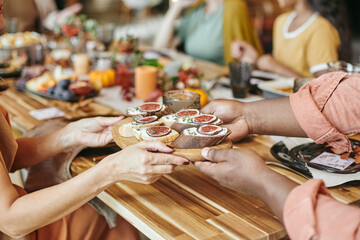 Hands of young Caucasian woman passing tasty homemade sandwiches to her African husband by served festive table during family dinner