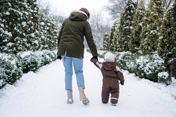 Winter walks with babies and young children. Baby toddler in Winter, How to Protect kids in Cold Weather. Mother and baby girl daughter walking in the winter park