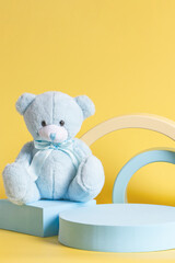 Creative baby kid toy background. Teddy bear and geometric shapes podium platform on yellow...