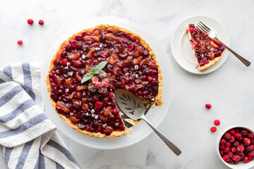 Top down view of a cranberry tart with one slice on a plate. 