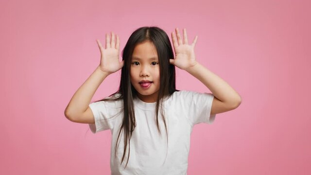 Asian Kid Girl Grimacing Holding Hands Near Temples, Pink Background