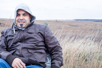 Naklejka na ściany i meble Happy man sitting in the middle of a praire in the Flint Hills enjoying the fresh air and cool breeze while wearing a brown jacket and blue jeans.