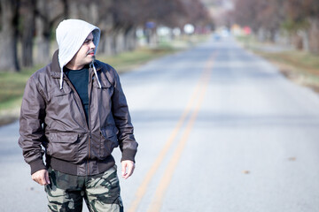 Cool guy looking outdoors in an empty street with a brown jacket and camo pants.