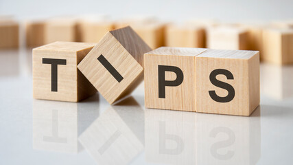 four wooden blocks with the letters Tips on the bright surface of a gray table, business concept