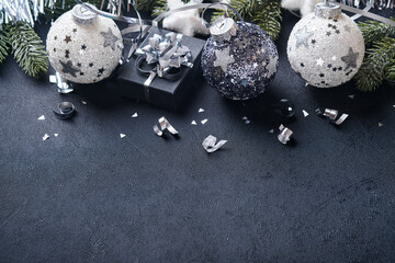 Christmas or New Year concept with black and silver baubles ball, gift box and champagne  with decorated silver metallic ribbon on black background. Happy New Year 2022. Mock up.