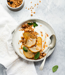 Greek yogurt with caramelized pear, granola, nuts and melted sugar for a wholesome breakfast on a gray ceramic plate. Rustic style. Top view