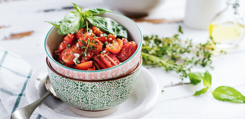 Baked cherry tomato with garlic, thyme and basil in vintage ceramic bowls on a light wooden table. Top view