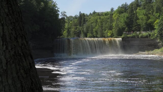 Medium View of Higher Falls of Tahquamenon Falls; rushing water drops into pool below, trees frame the banks; low angle.