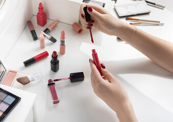 open red lip gloss in hands of girl on white dressing table against background of other lipsticks. Lipstick and lip gloss concept for makeup