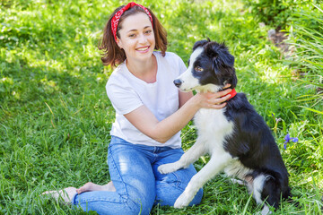 Smiling young attractive woman playing with cute puppy dog border collie in summer garden or city park outdoor background. Girl training trick with dog friend. Pet care and animals concept