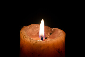 A thick candle with light burning in the darkness.
