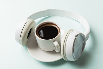 Cup of coffee and headphone on light blue background