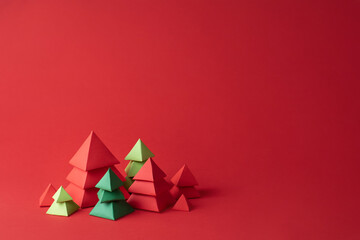 Red and green paper christmas trees on red background.