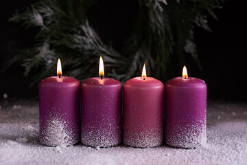 Four burning pink and purple advent candles on snow.