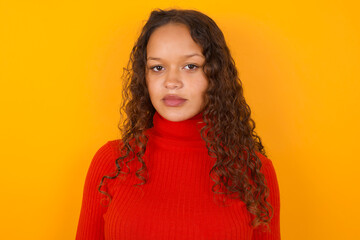 Joyful Teenager girl with curly hair wearing red sweater over yellow background looking to the...