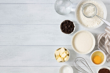 Ingredients for baking background copy space. Baking ingredients: white flour, butter, baking powder, chocolate, sugar, ice water on a white wooden background, copy space, top view.