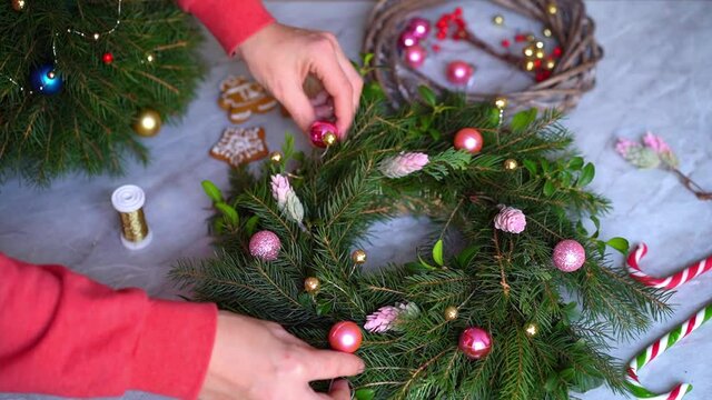 Making rustic christmas wreath. Hands decorate a Christmas wreath with pink round toys. Close-up. Making crafts. Seasonal holiday workshop online, making festive decorations at home. Selected focus.