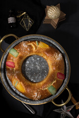 Overhead view of a Roscón de Reyes, King Cake, with some Christmas ornaments around over dark and elegant background.